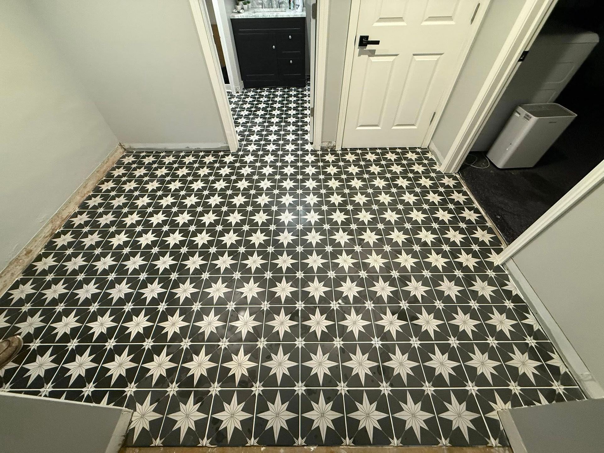 Bathroom with black-and-white patterned floor tiles and a mirror reflecting the hallway.