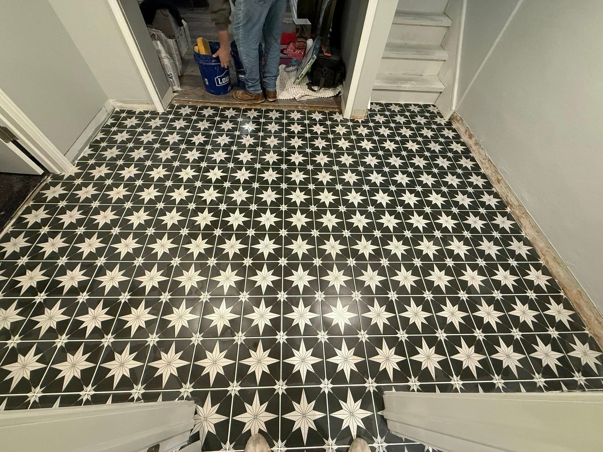 Black-and-white star-pattern tile floor in a hallway, with a doorway opening to a cluttered room.