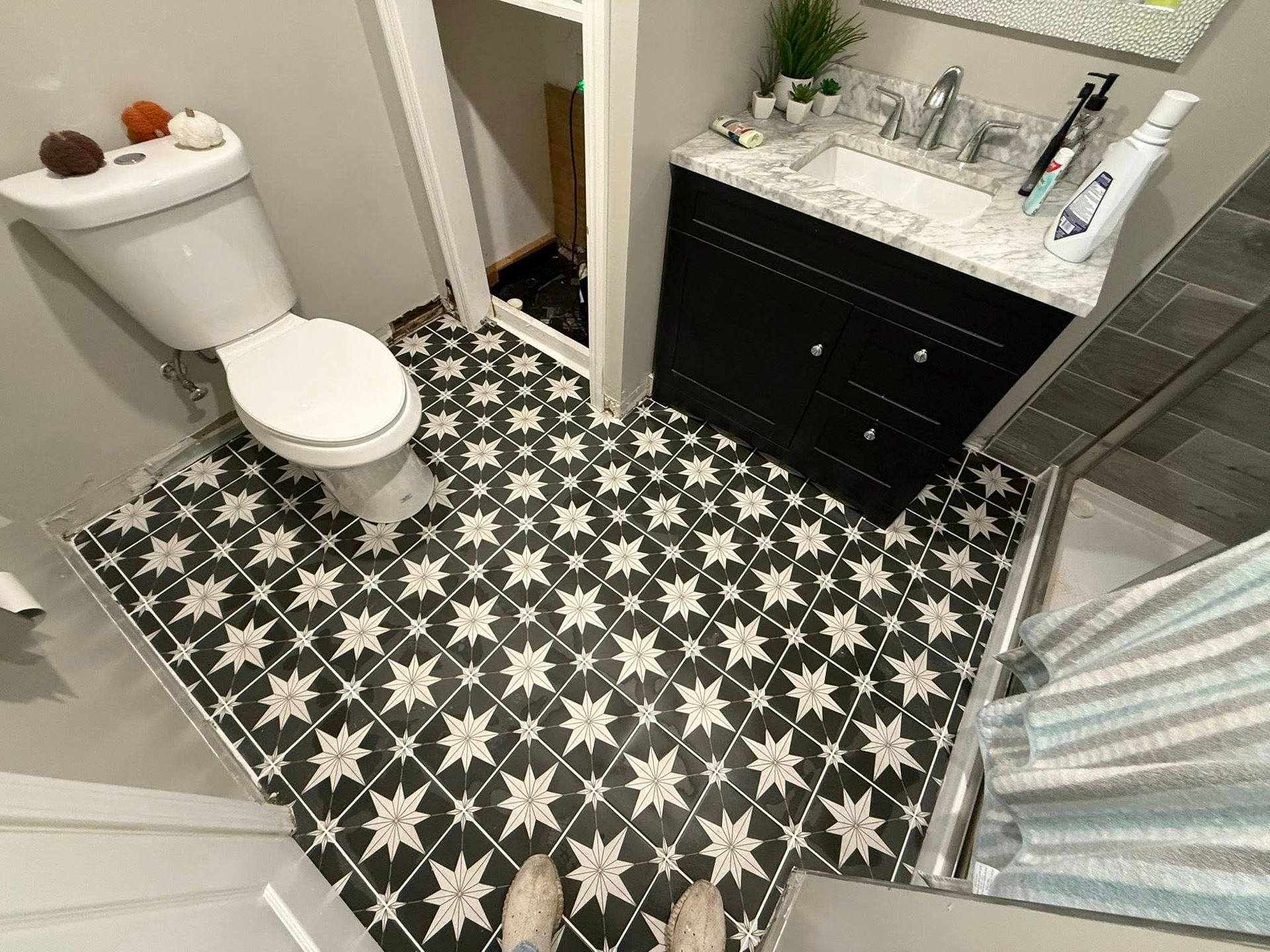 Small bathroom with black-and-white patterned tile, white toilet, dark vanity, and shower stall.