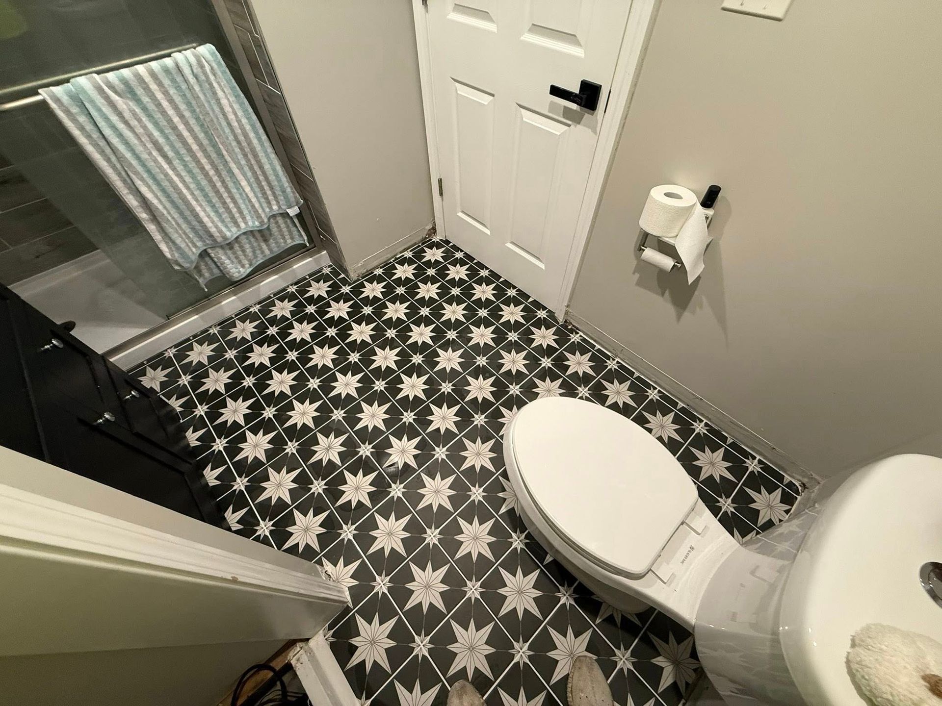 Small bathroom with black-and-white patterned floor, white toilet, towel rack, and shower curtain.