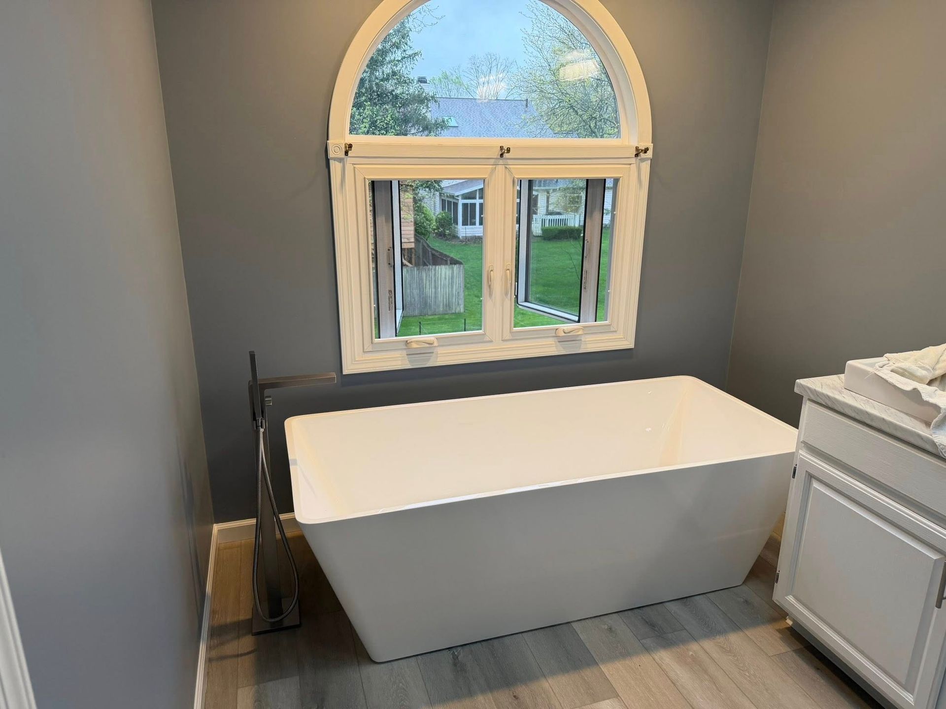 Modern bathroom with a freestanding white tub beneath an arched window.