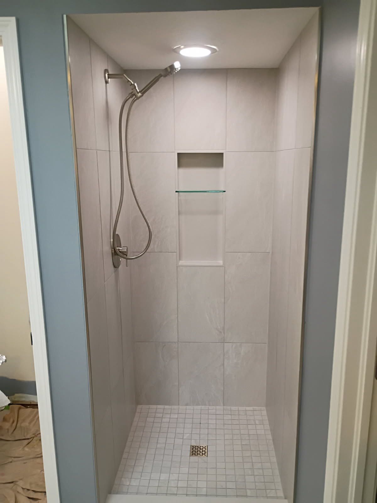 Empty tiled walk-in shower with handheld showerhead and recessed shelf.