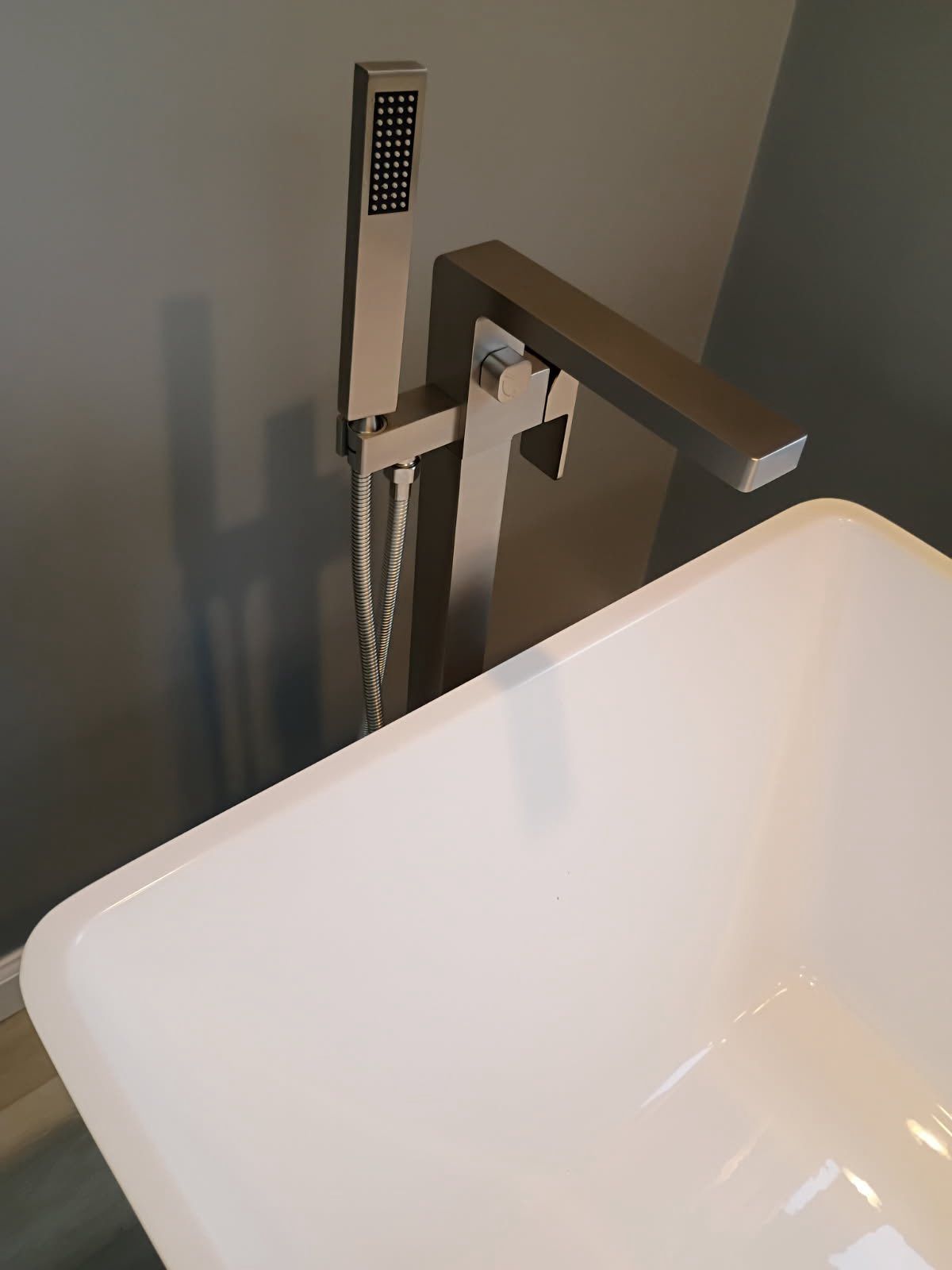White sink basin beside a chrome faucet and handheld sprayer in a bathroom.