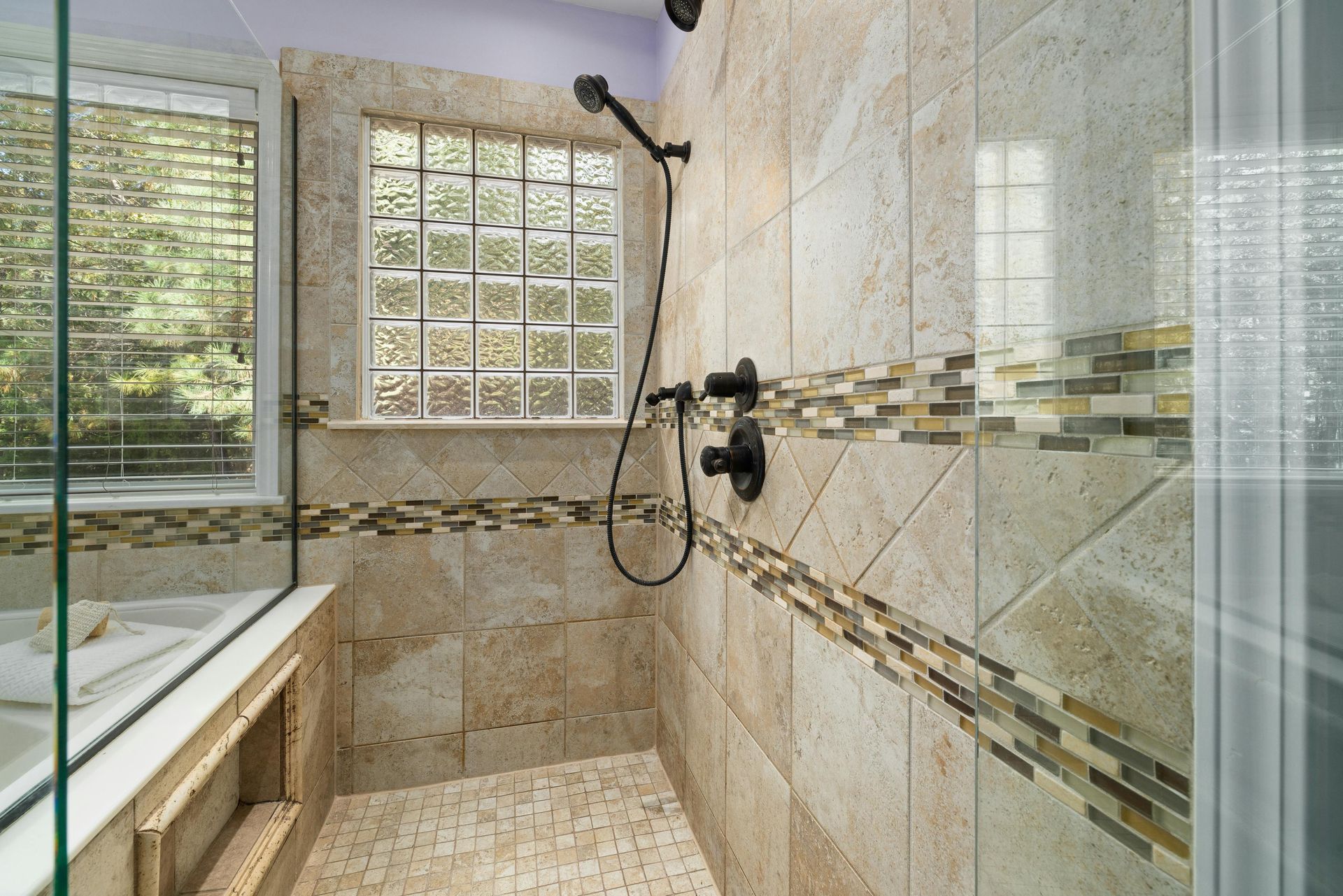 Luxury beige-tiled bathroom with glass shower, rain showerhead, and a window by the tub
