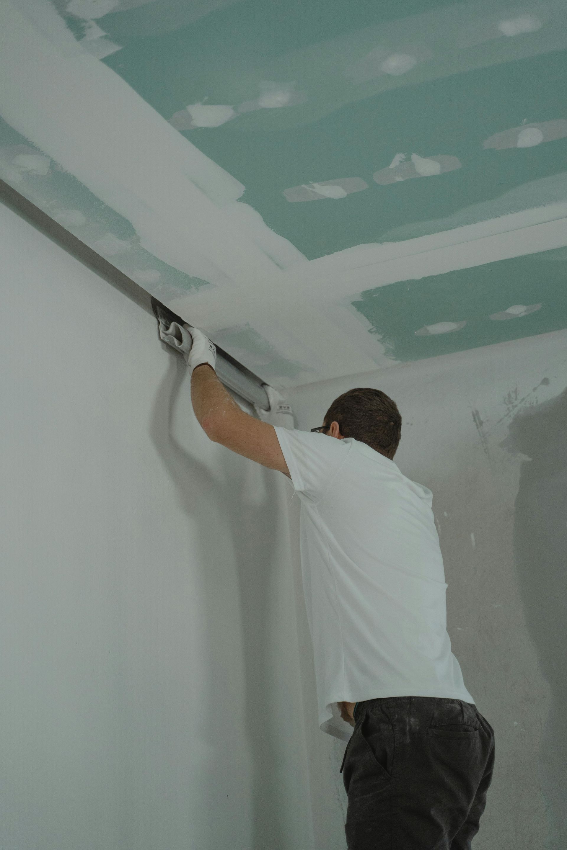 Person sanding drywall on a ceiling during home renovation.