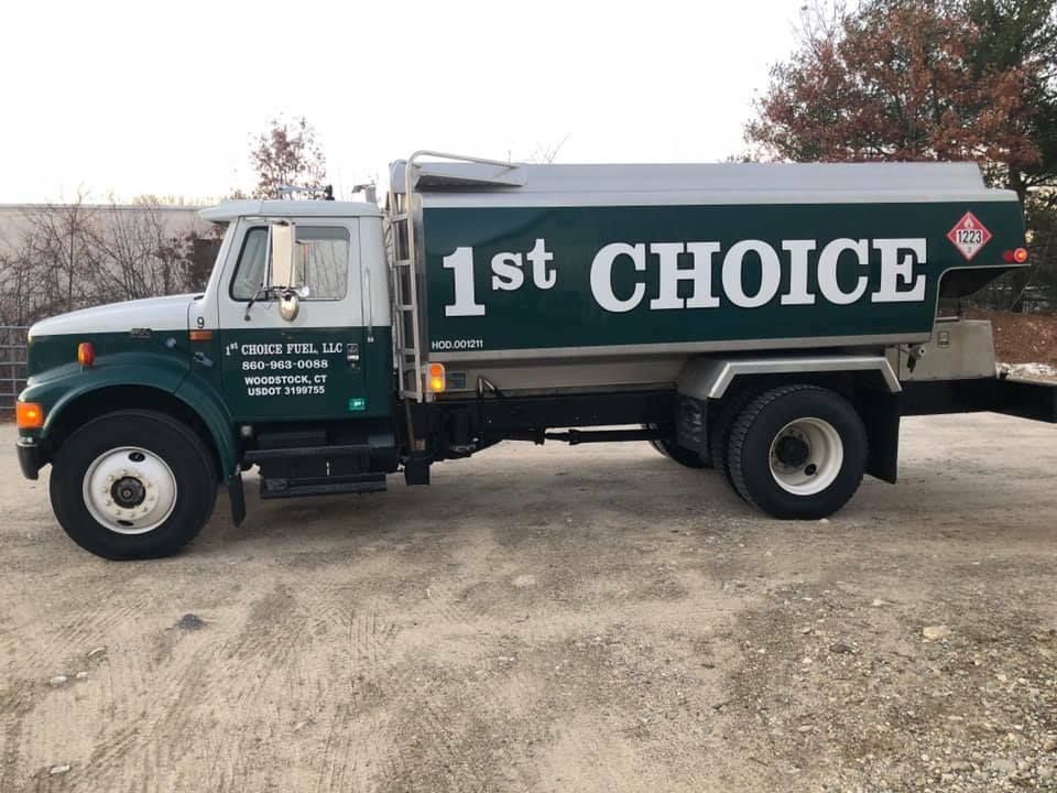 Green and white 1st Choice tanker truck parked on gravel.