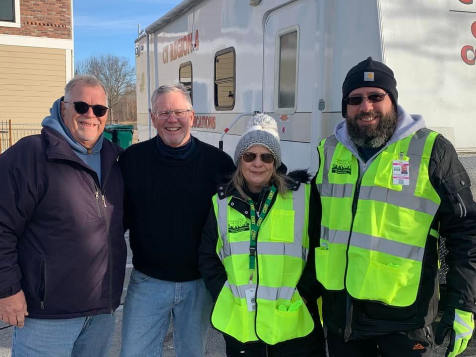 Four people in front of a mobile medical unit. Two wear reflective vests. Outdoors, smiling.