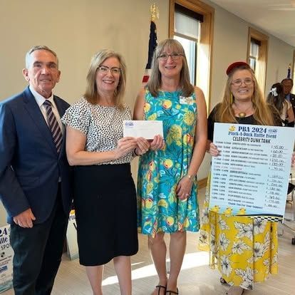 Four people holding a check and a sign. Woman in floral dress presents a check with others.