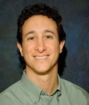 Smiling man with dark, curly hair wearing a green button-down shirt.