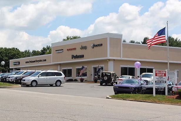 Car dealership with cars parked out front and an American flag flying.
