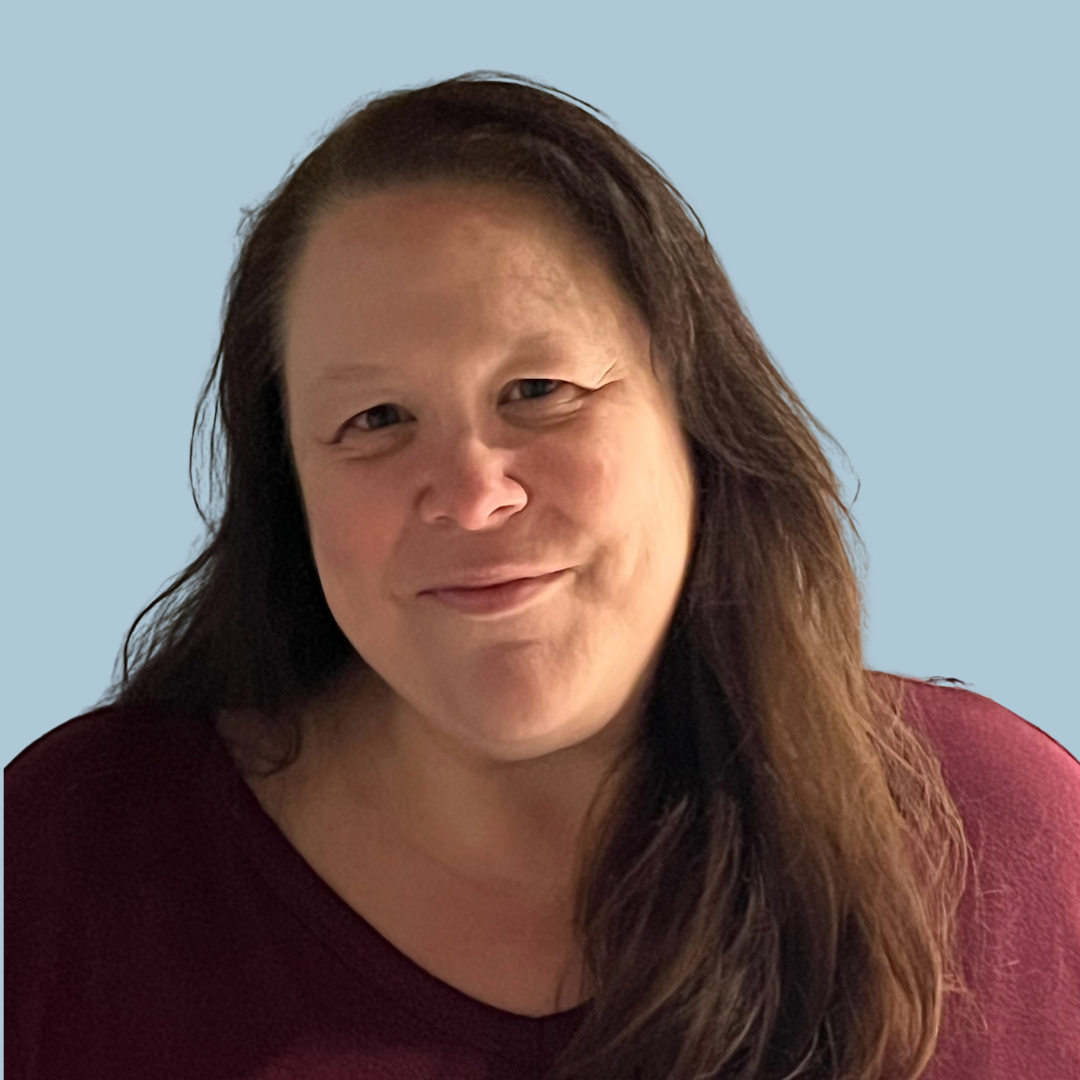 A woman with long hair is smiling and wearing a red shirt.