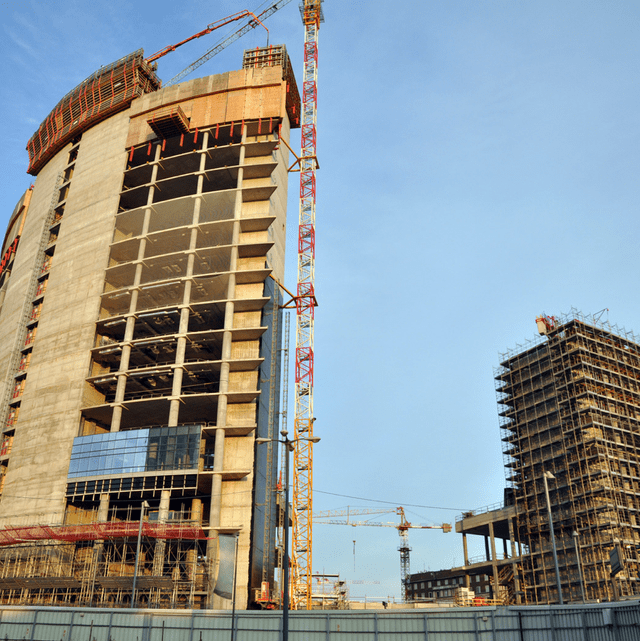 Construction site: tall, unfinished buildings with cranes against a blue sky.