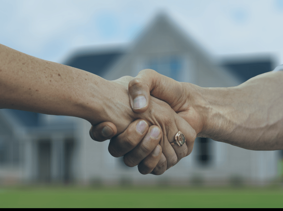 Two people shaking hands with a house in the background