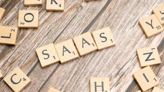 The word saas is written in scrabble tiles on a wooden table.