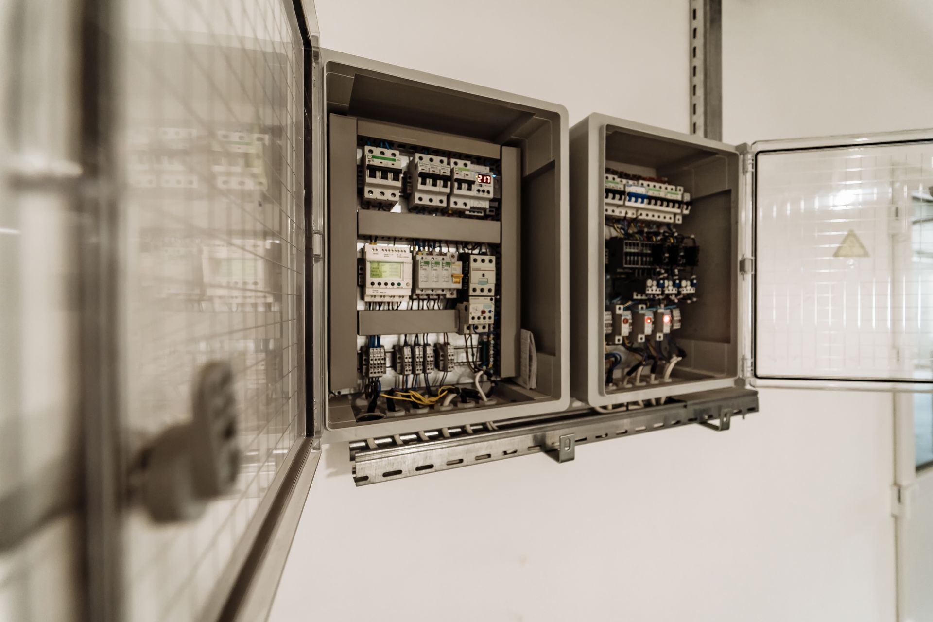 Open electrical control cabinets with circuit breakers, relays, and wiring mounted on a white wall.