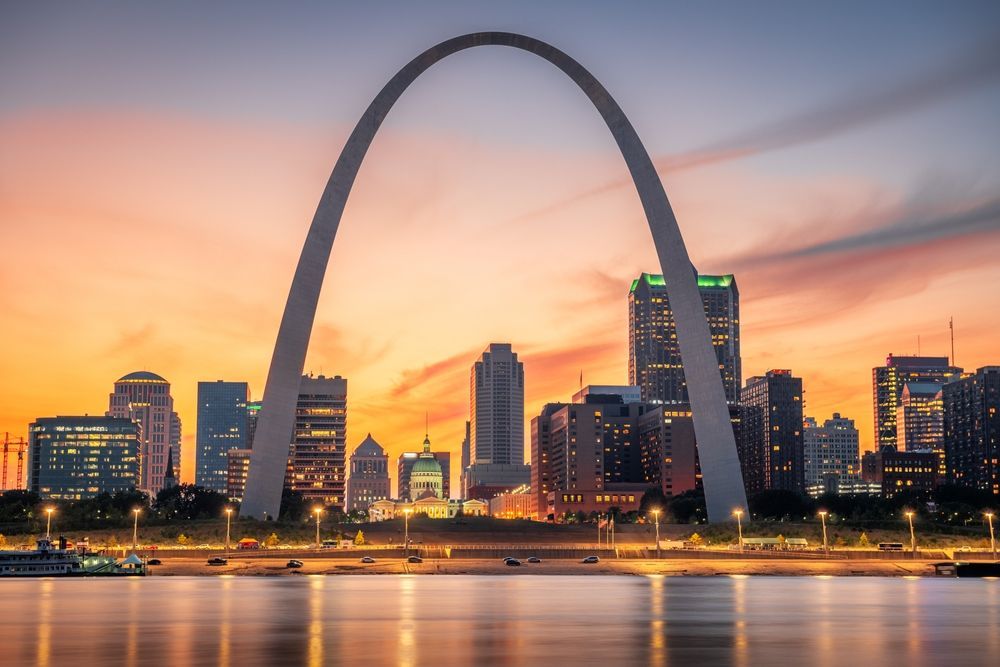 The Gateway Arch in St. Louis against an orange and pink sunset; city skyline visible.