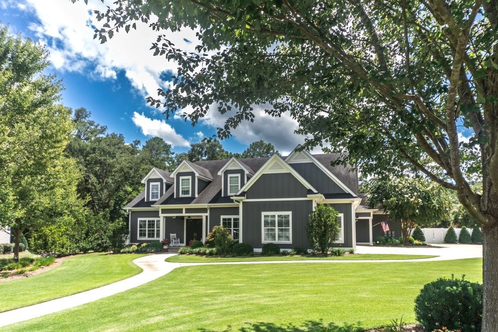 Dark gray house with white trim, green lawn, trees, and blue sky.