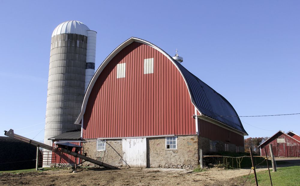 Red barn and silo against a clear blue sky on a farm.