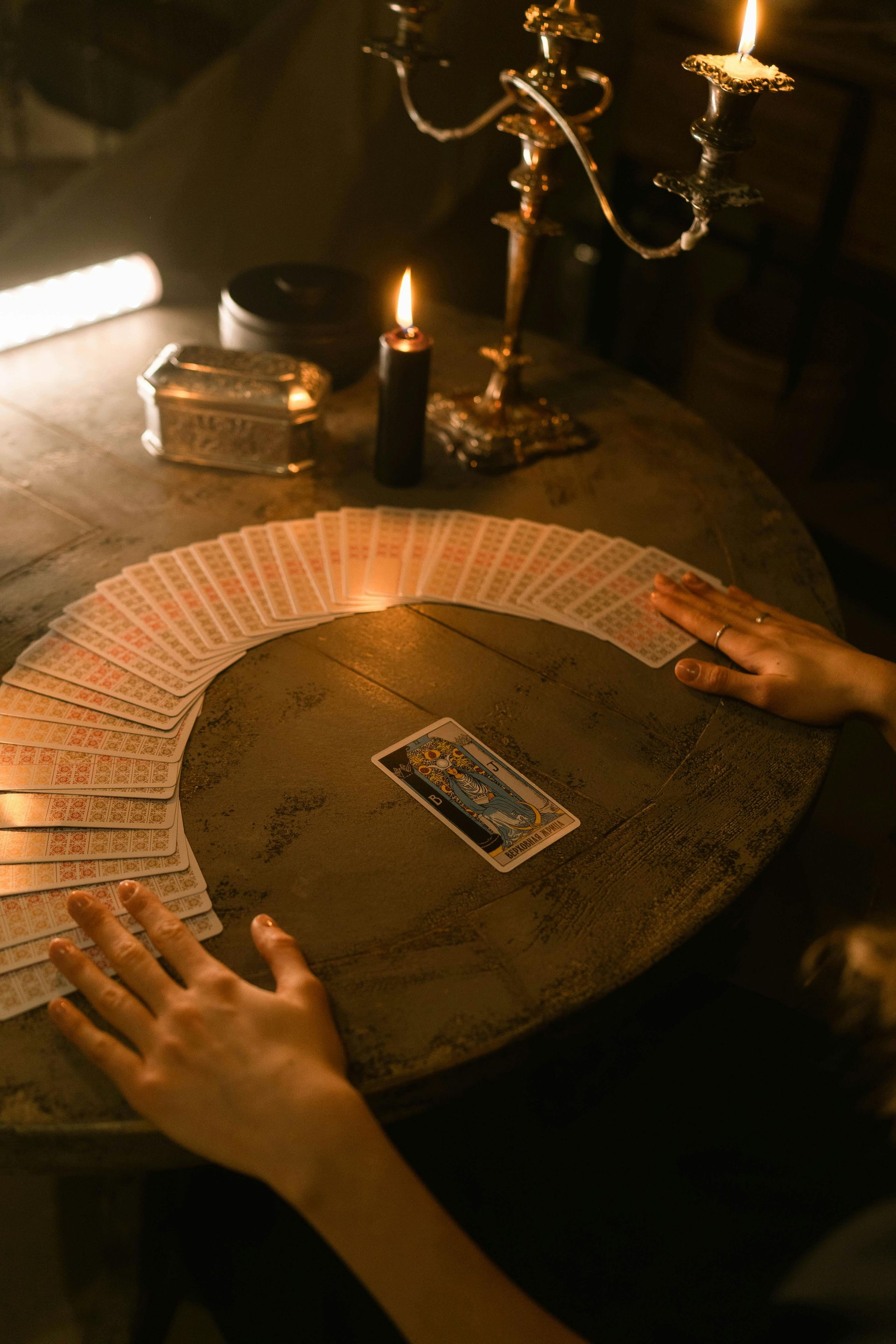 Woman's hand with tattoo and red nails laying tarot cards on a wooden table with crystals and lavender.