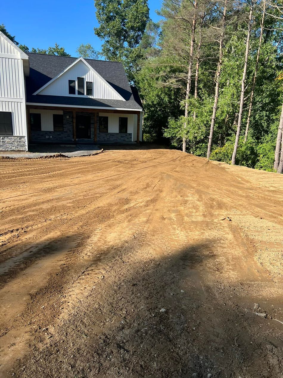 House with graded dirt yard, trees in background, sunny day.