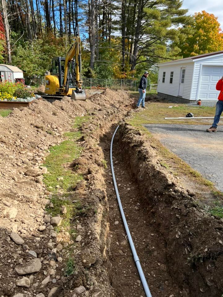 A yellow tractor tilling a field under a cloudy sky. Bare trees and power lines are visible in the distance.