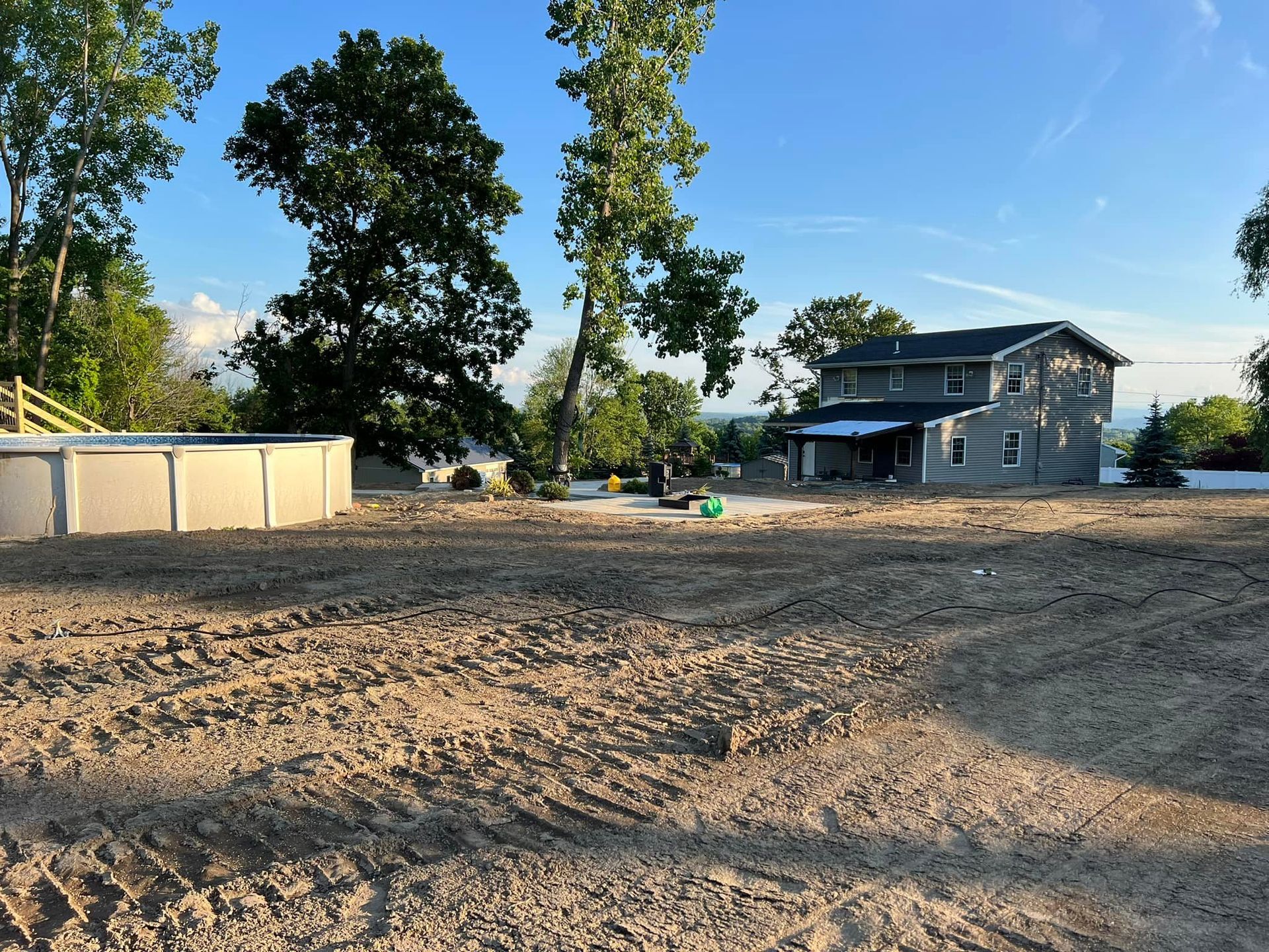 Dirt lot with an excavator, trees, and green grass.