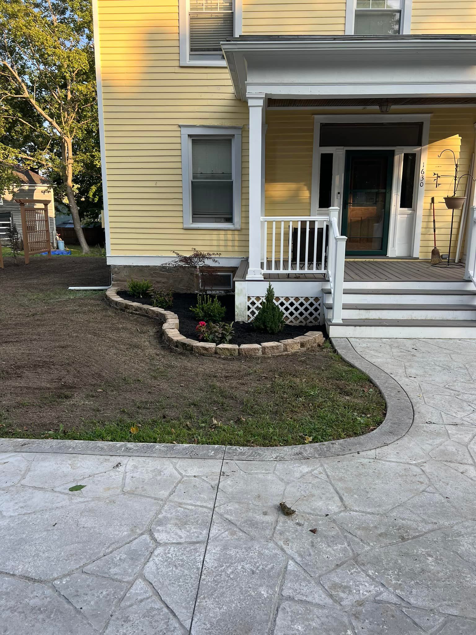 Yellow house with front porch, flower bed, and concrete walkway.
