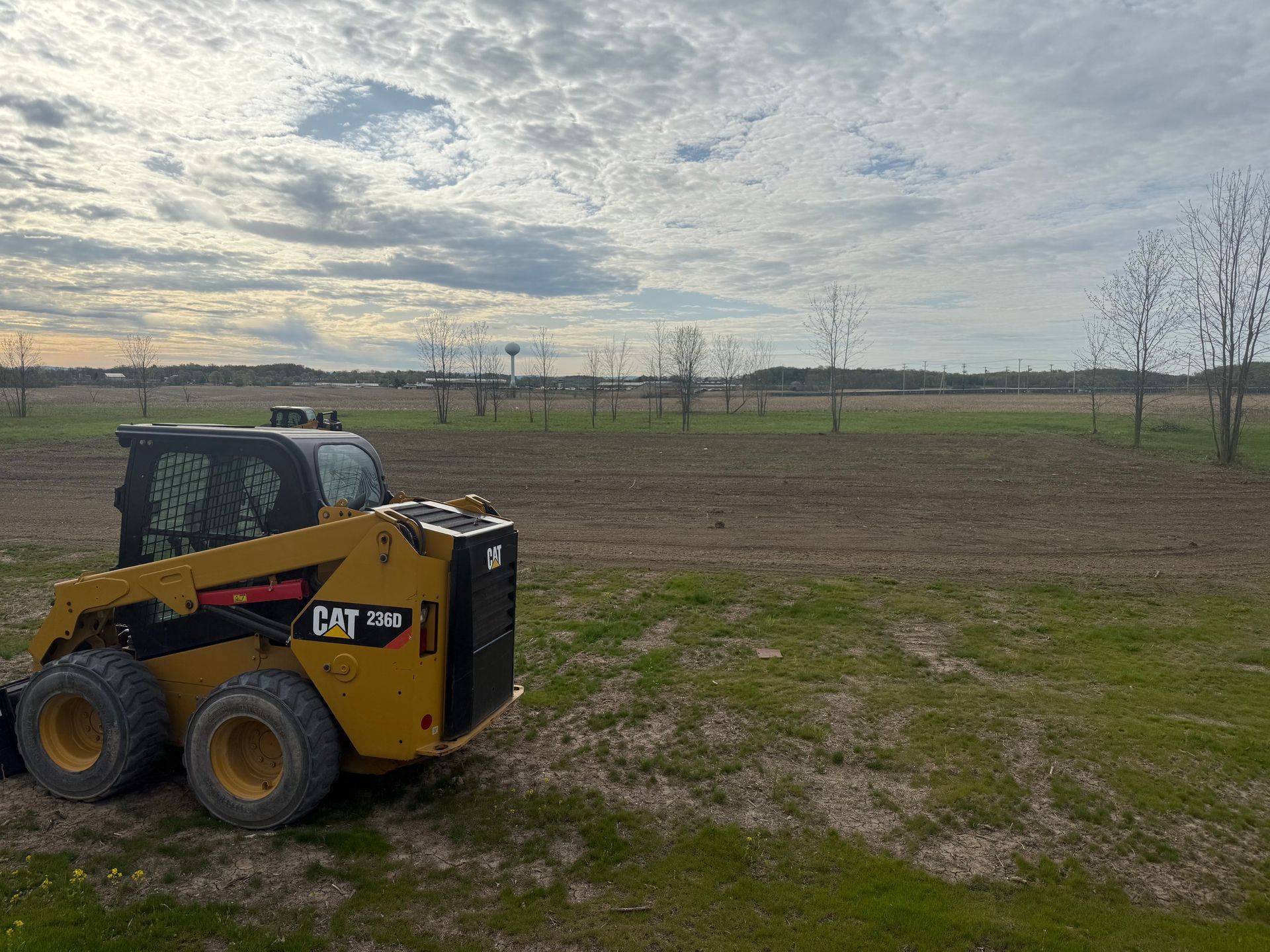 Yellow CAT skid steer on field, cloudy sky background.