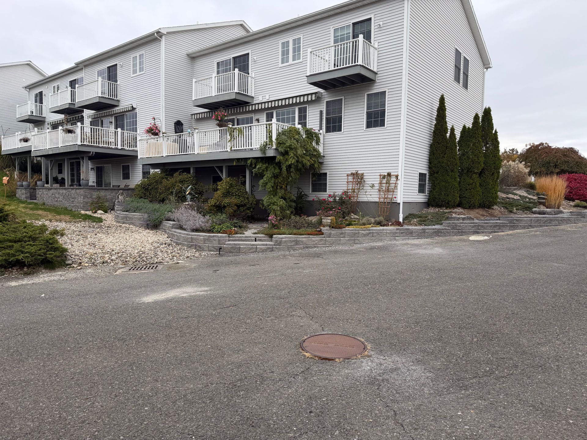Multi-story white building with balconies and rock landscaping in front. Gray gravel parking area.
