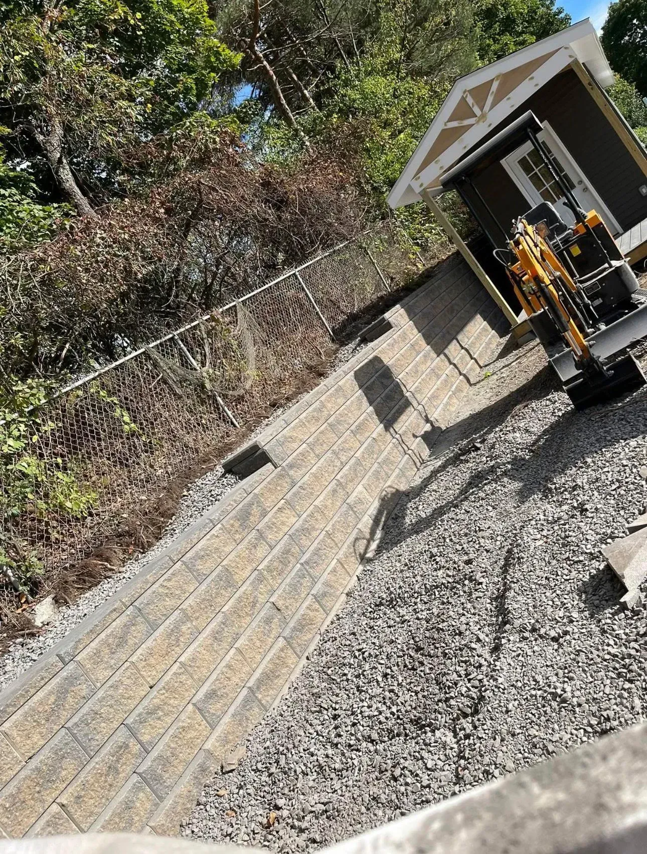 Retaining wall constructed with stone blocks, gravel base, small shed, and excavator.