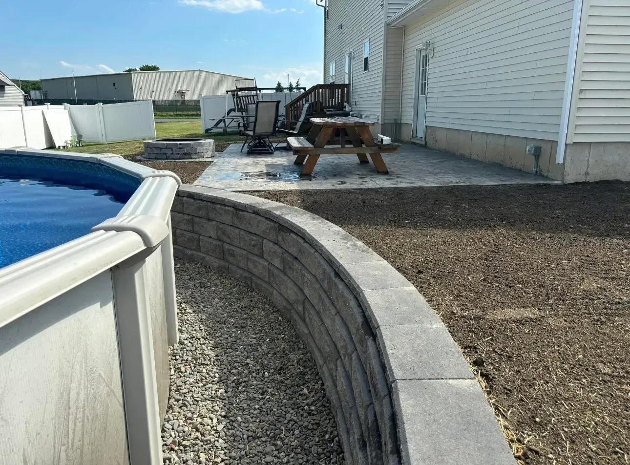 Backyard with an above-ground pool, retaining wall, patio, picnic table, and fire pit.