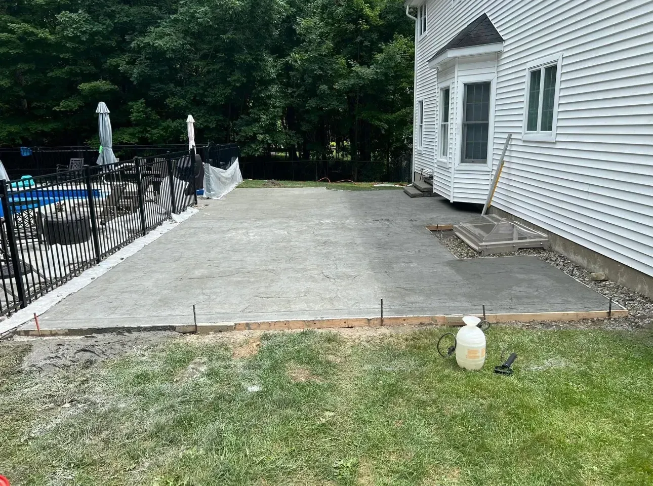 Newly poured concrete patio next to a house and pool.