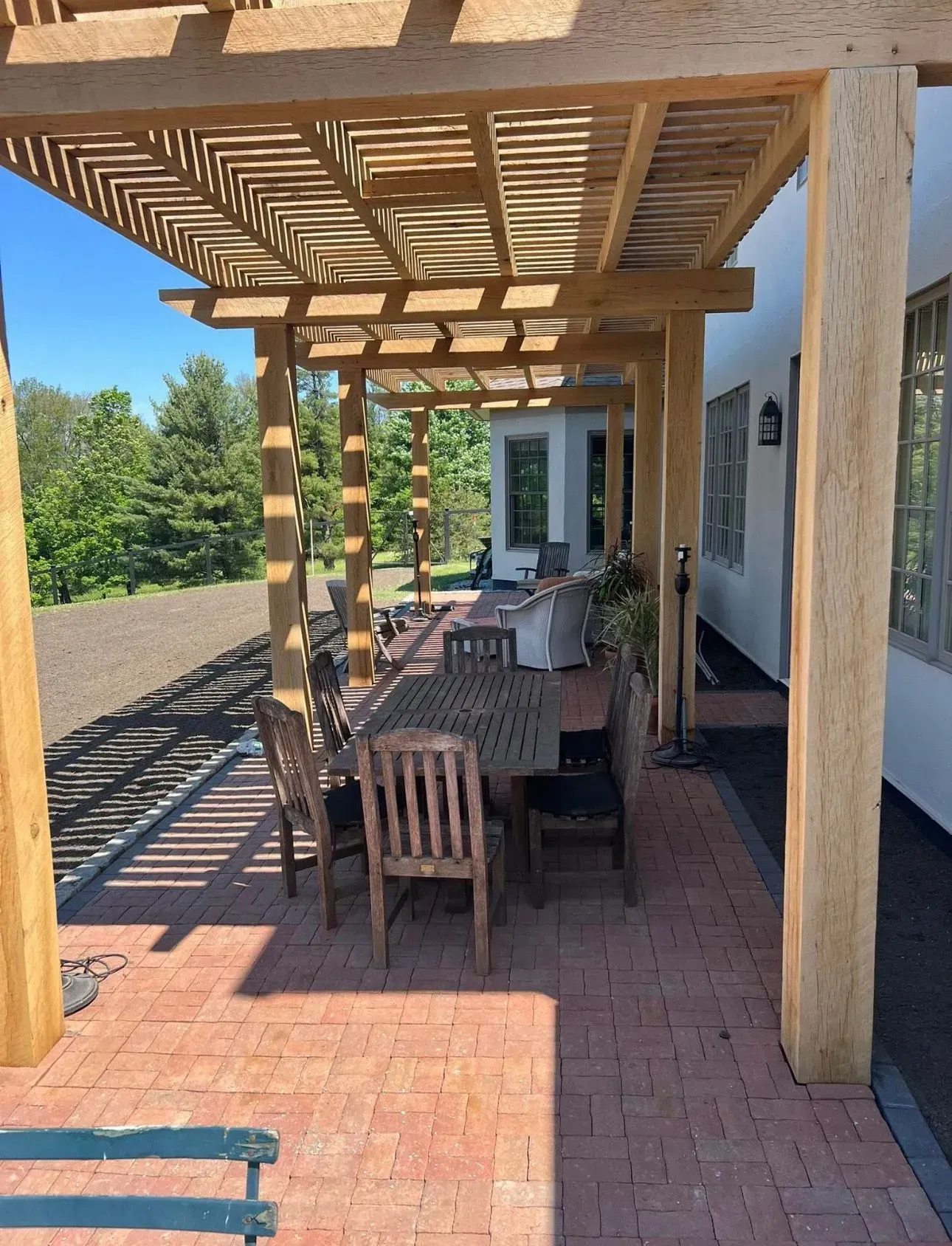 Wooden pergola over a brick patio with a table and chairs. A house is visible in the background.