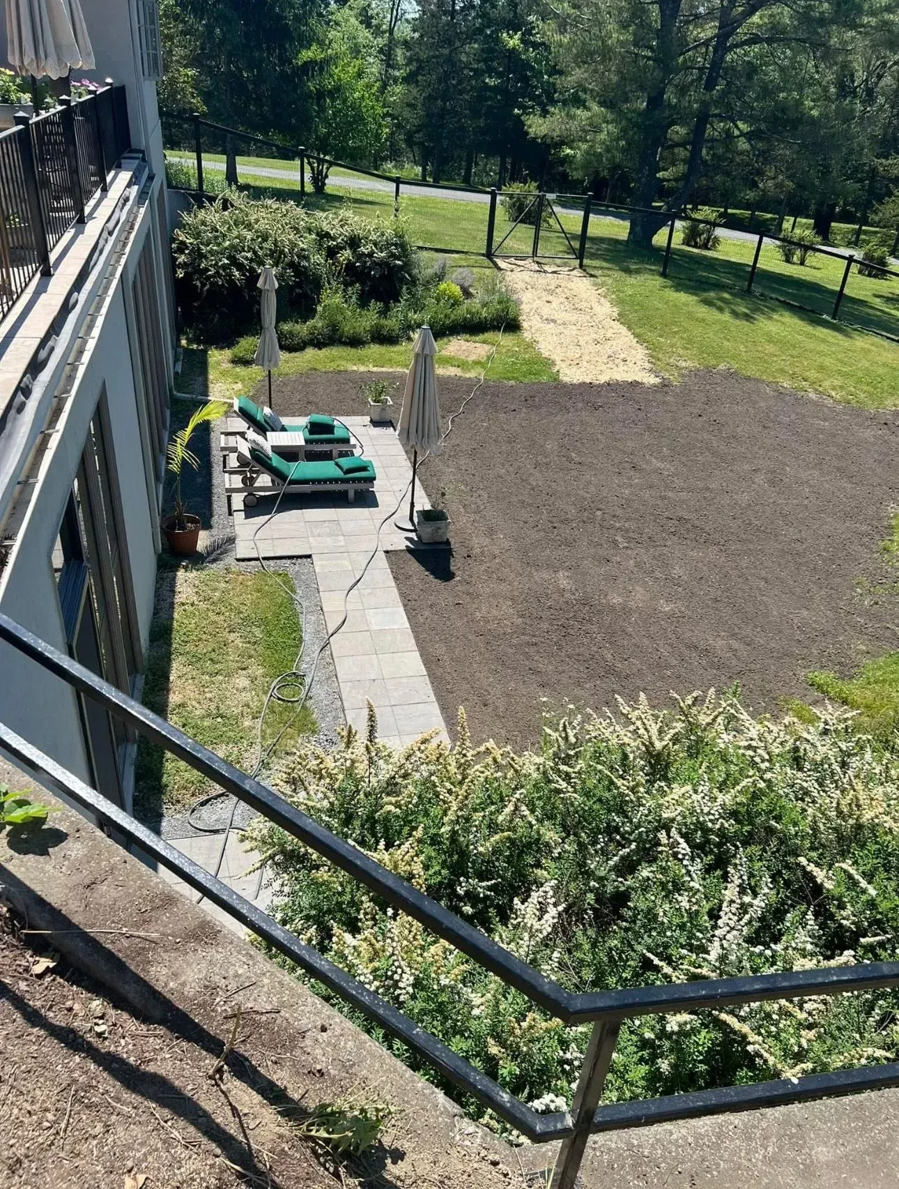 Outdoor patio with lounge chairs, umbrellas, and newly tilled soil in a sunny garden.