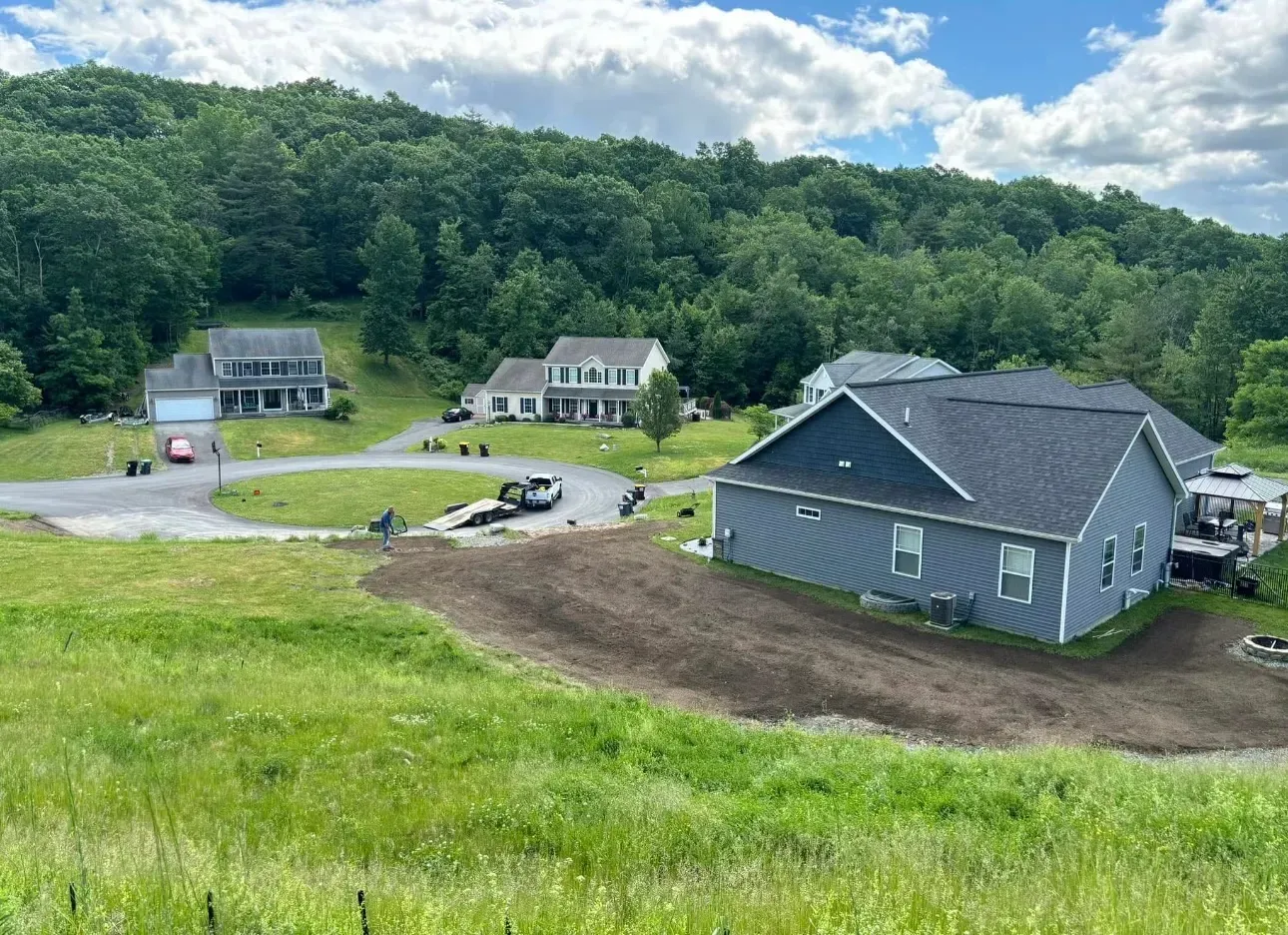 Houses and a construction site at the base of a forested hill.