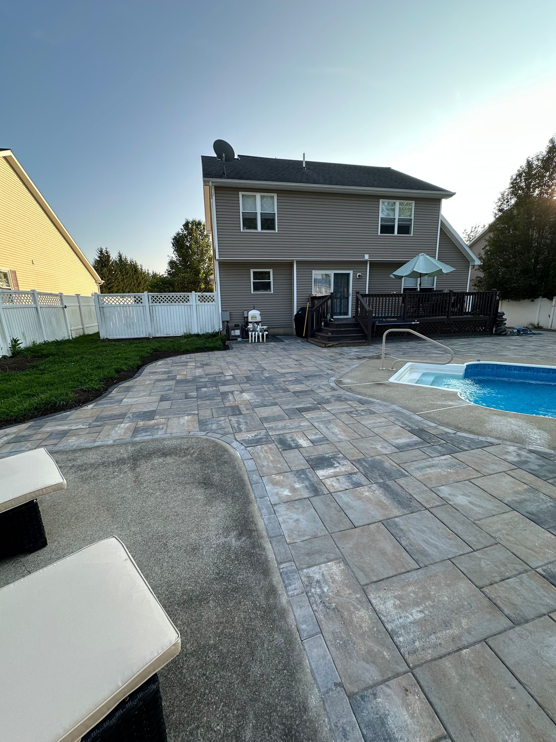 Patio with pavers and pool, backyard view of a two-story house with a deck.