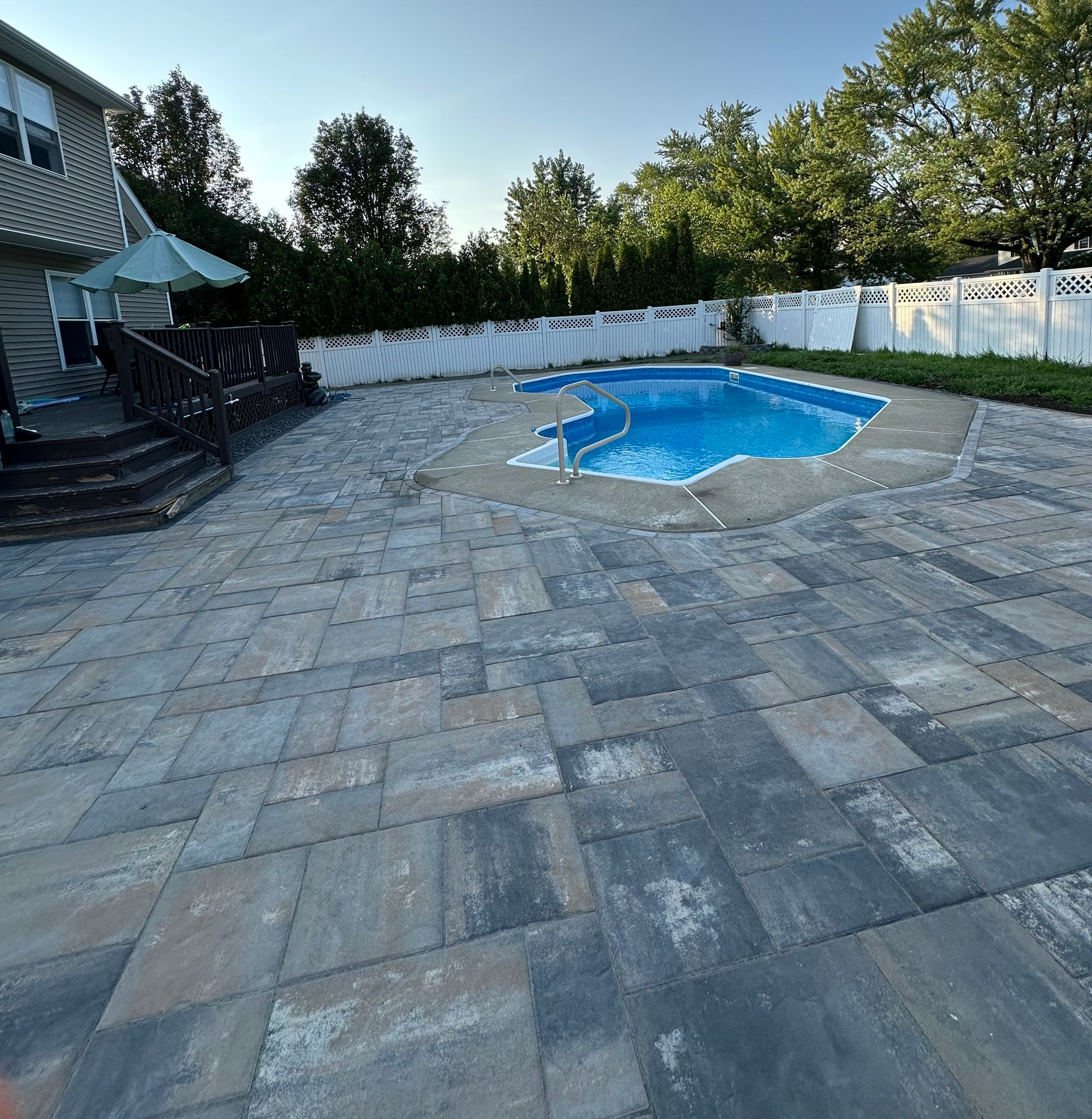 Pool equipment and patio with pavers next to a house with gray siding.