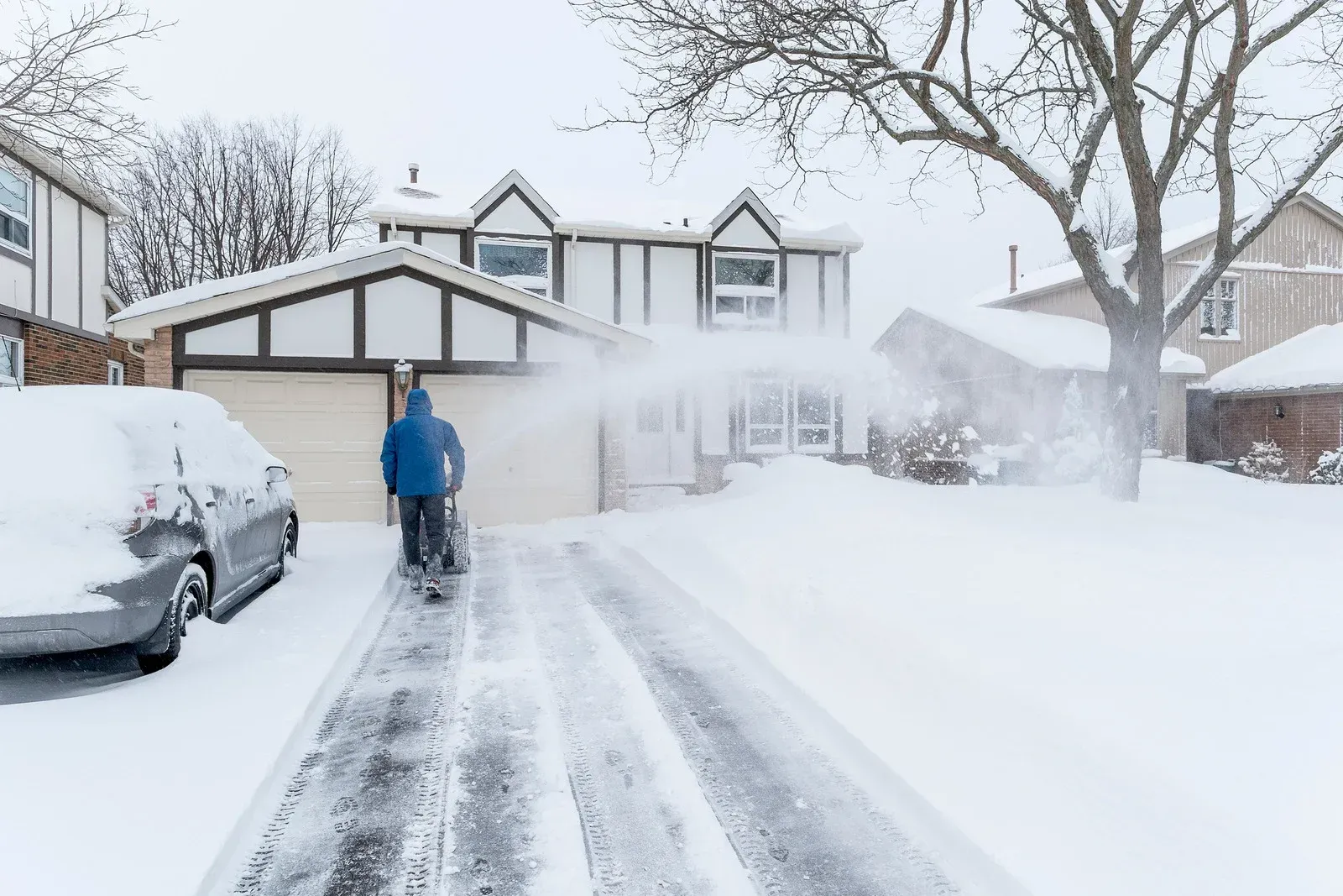 Yellow snowplow clearing snow in front of snow-covered buildings.