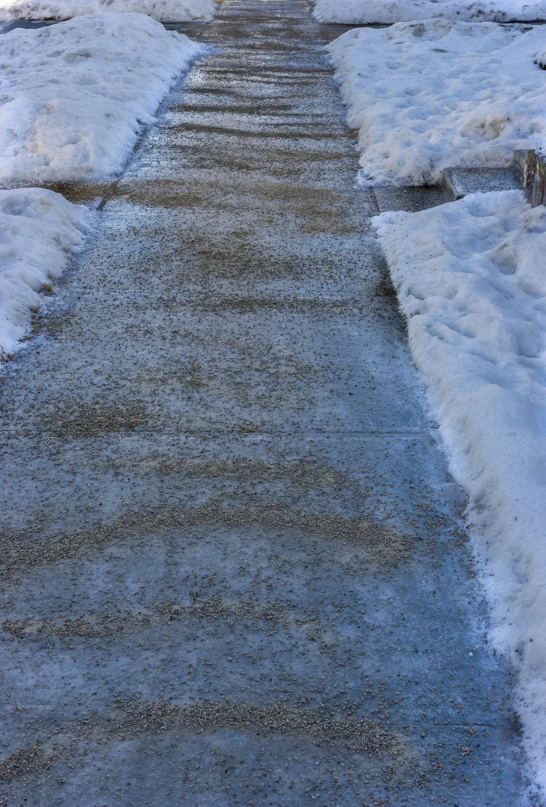Snowy sidewalk with salt granules, flanked by snowbanks.