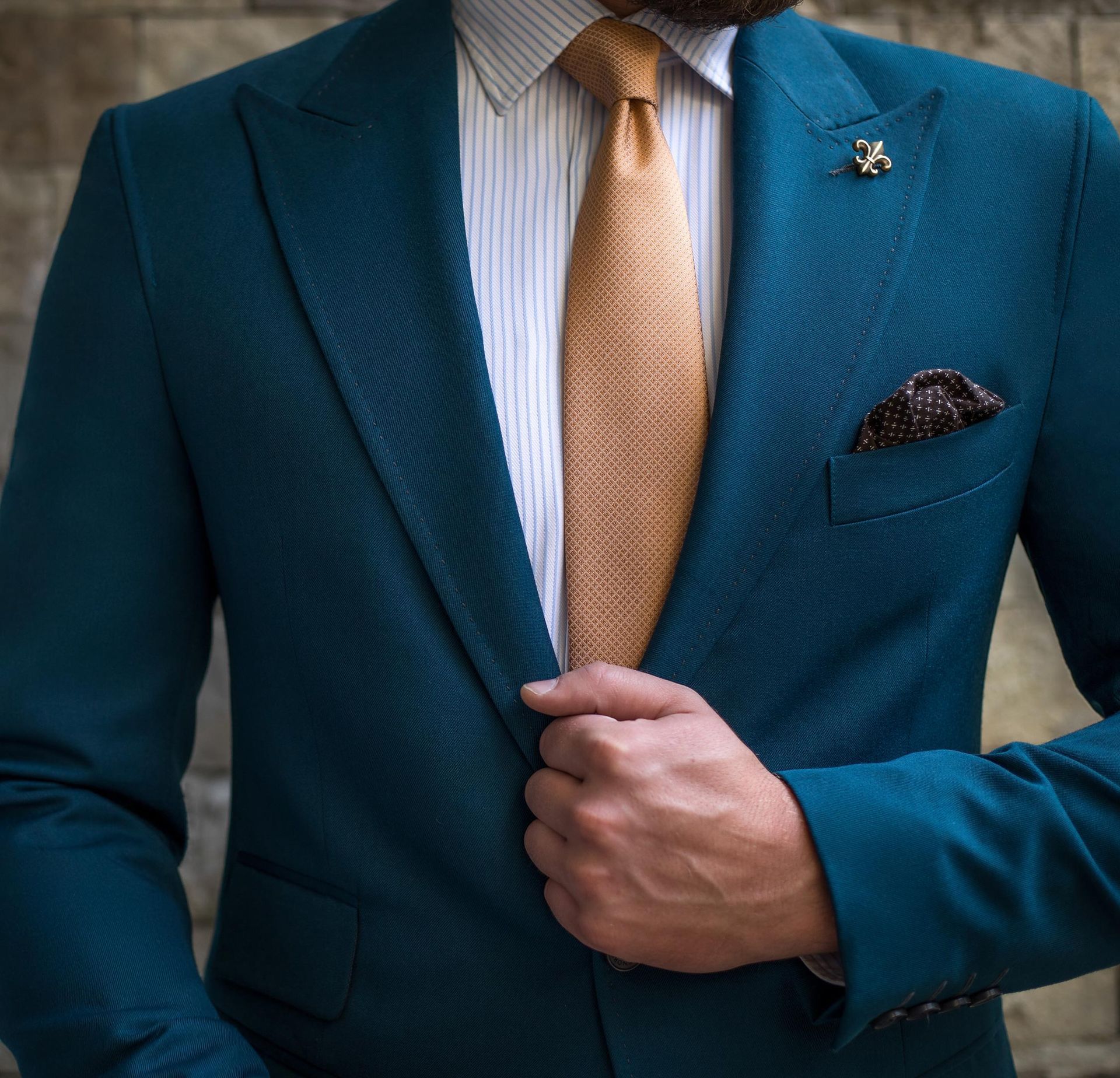 Man in teal suit, orange tie, striped shirt, and pocket square, adjusting jacket.