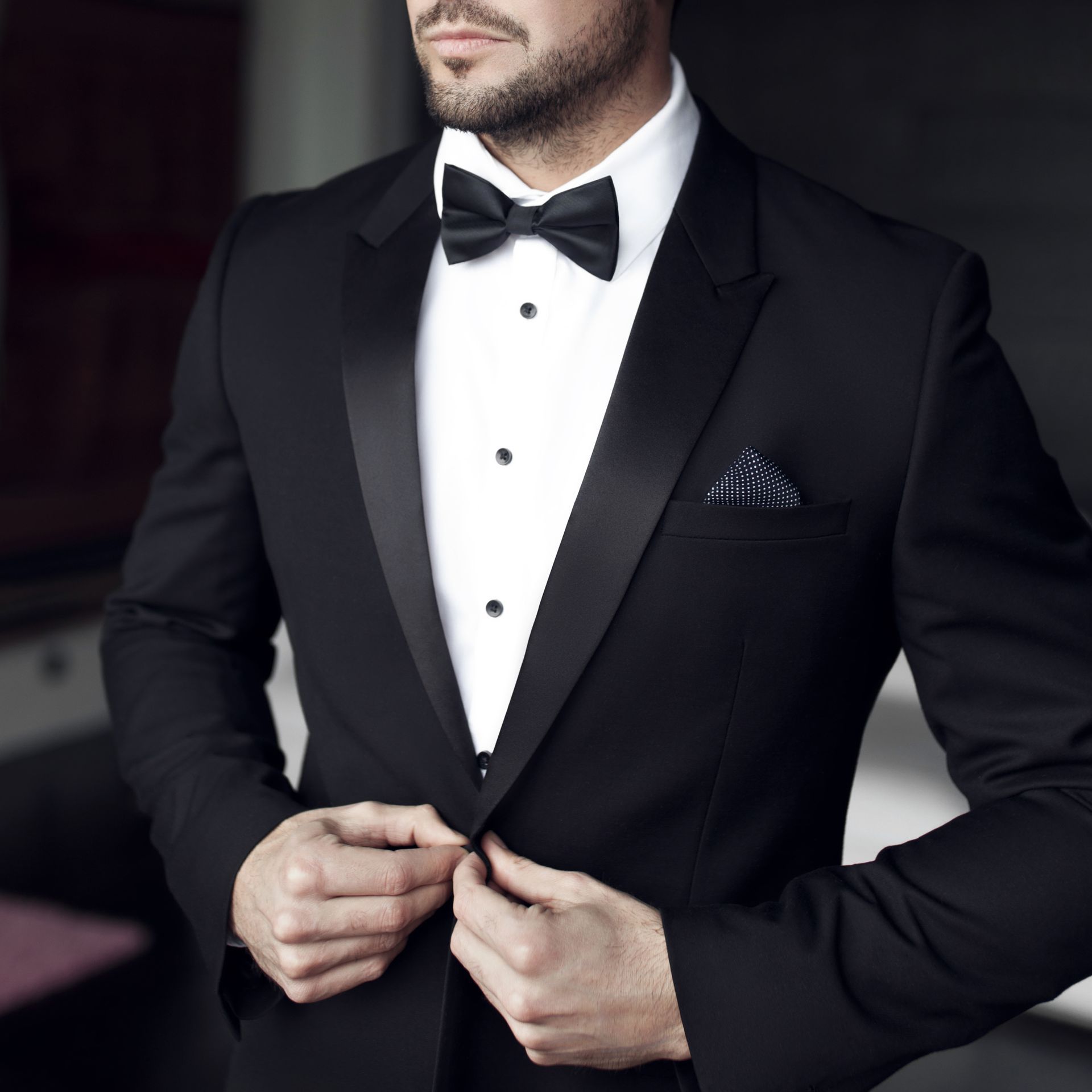 Man in black tuxedo adjusting jacket, white shirt, and bow tie.