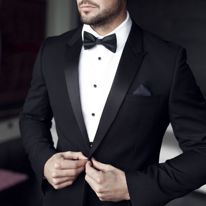 Man in black tuxedo adjusting jacket, white shirt, and bow tie.