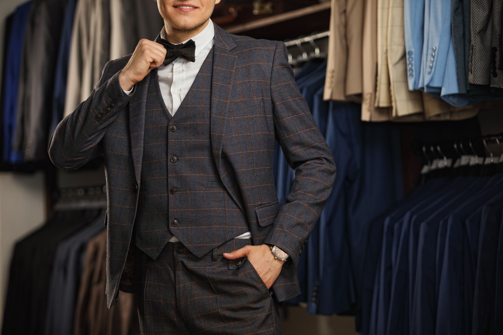 Man in suit adjusting bowtie, standing in a suit shop.