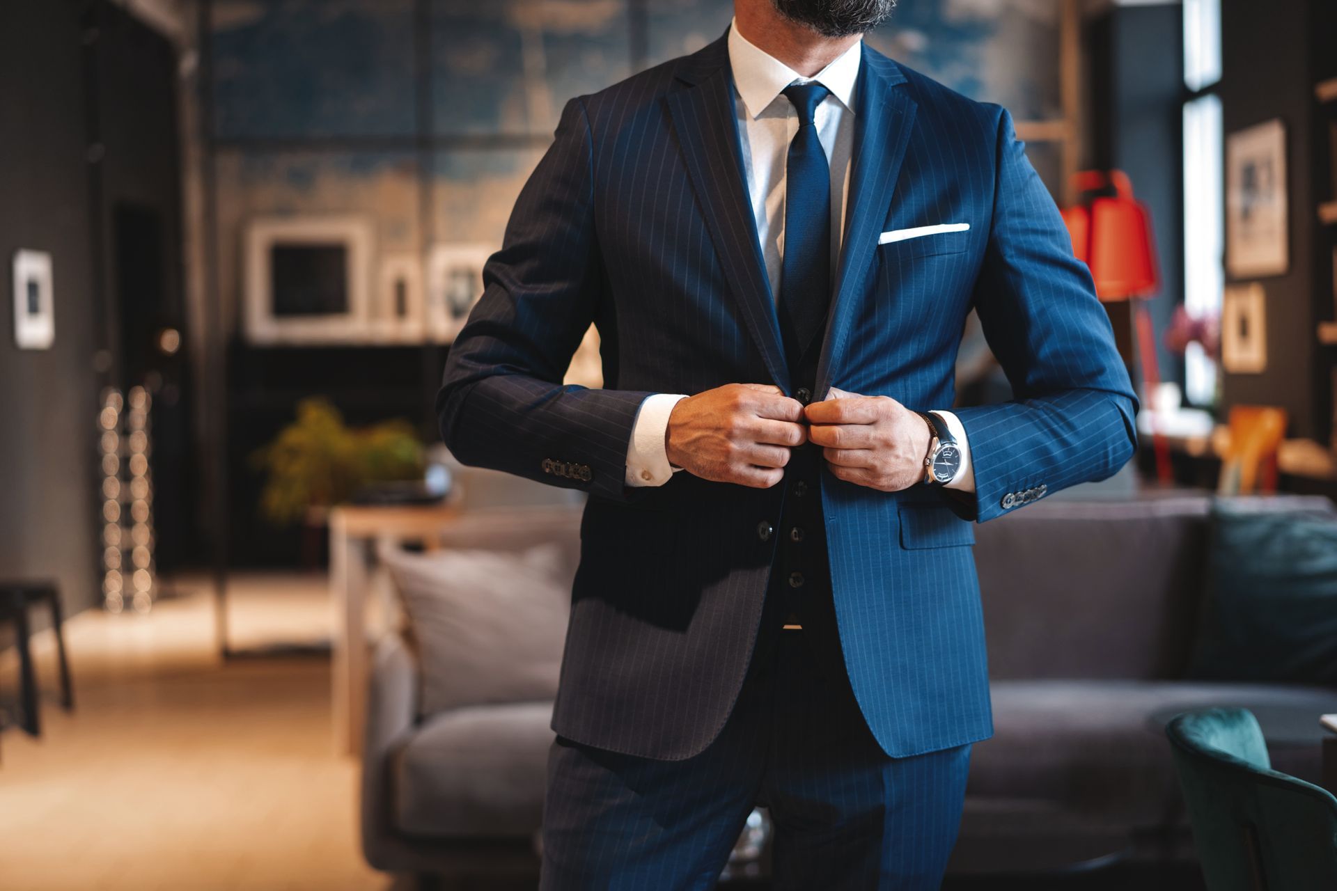 Man in blue suit buttoning his jacket in a stylish room.