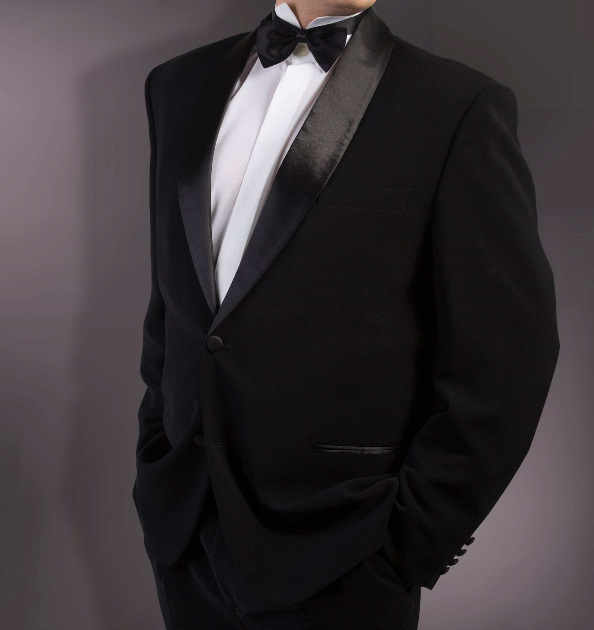 Black tuxedo jacket with satin lapels, white shirt, and bow tie. Hands in pockets.