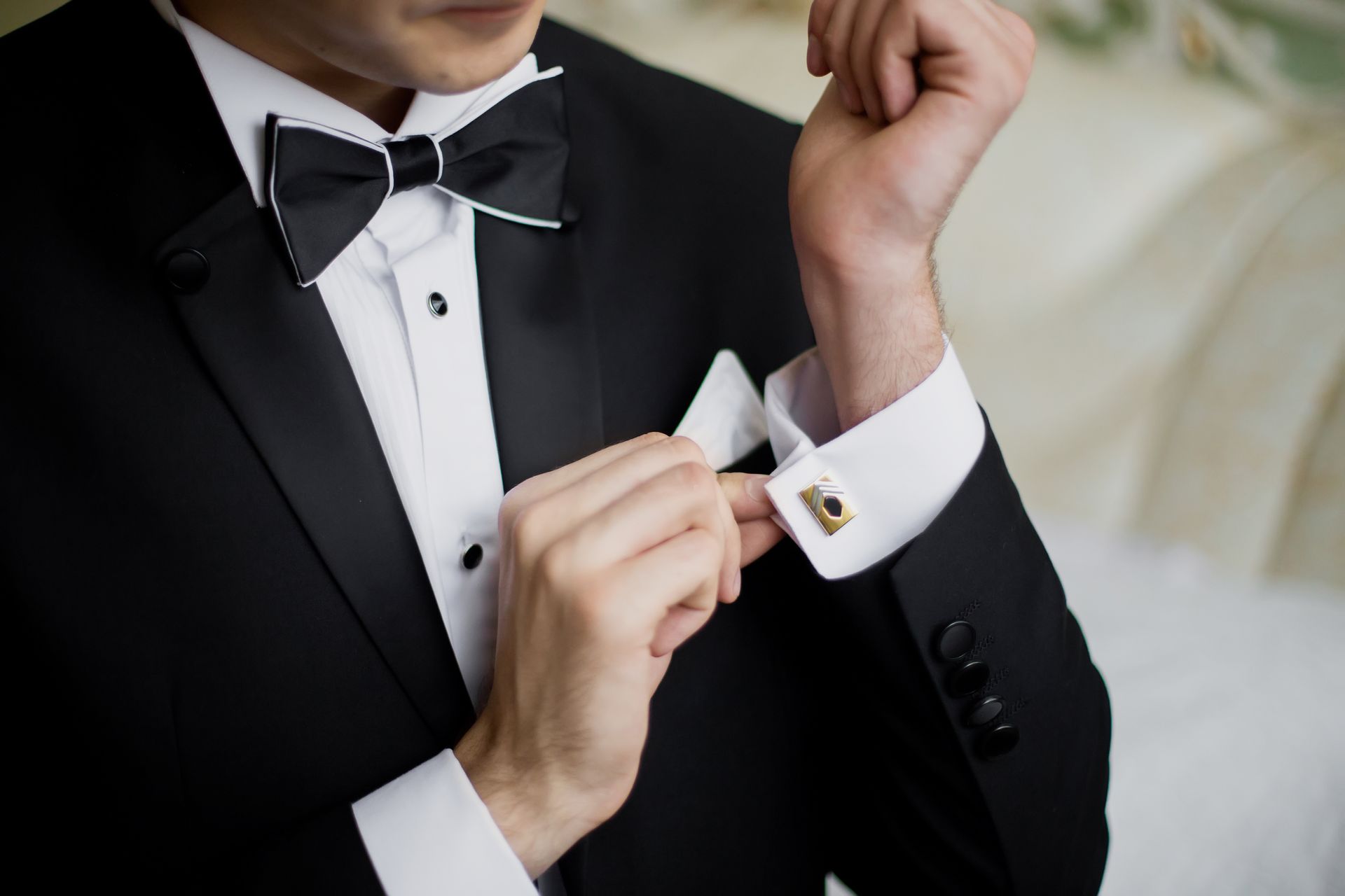 Man in tuxedo adjusts his cufflink, close-up shot, black jacket, white shirt and bow tie.