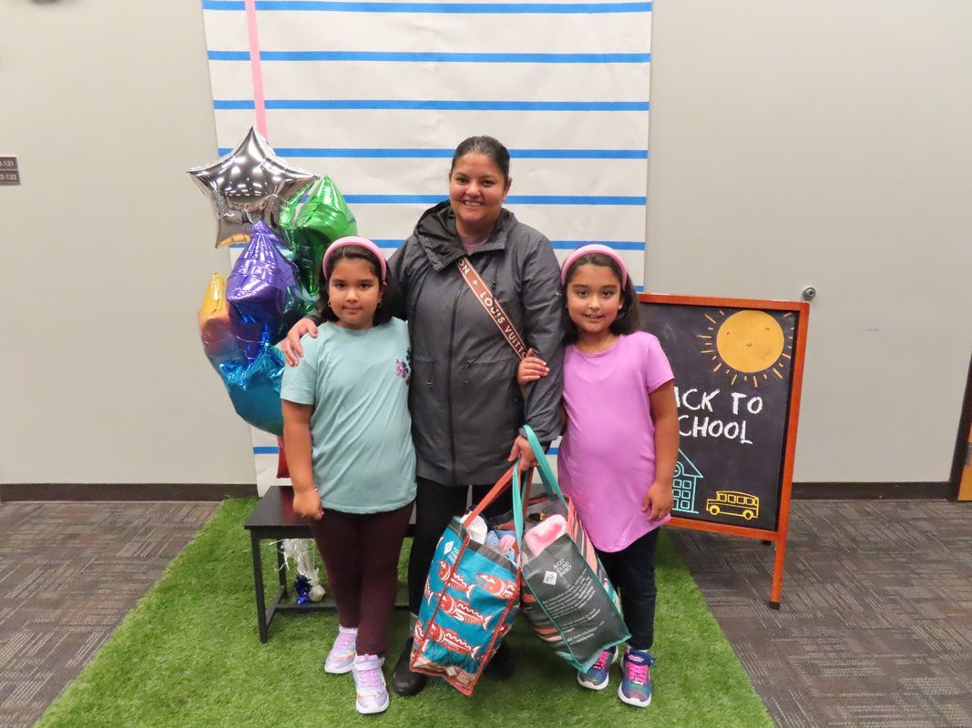 Woman and two girls posing with school supplies next to a 