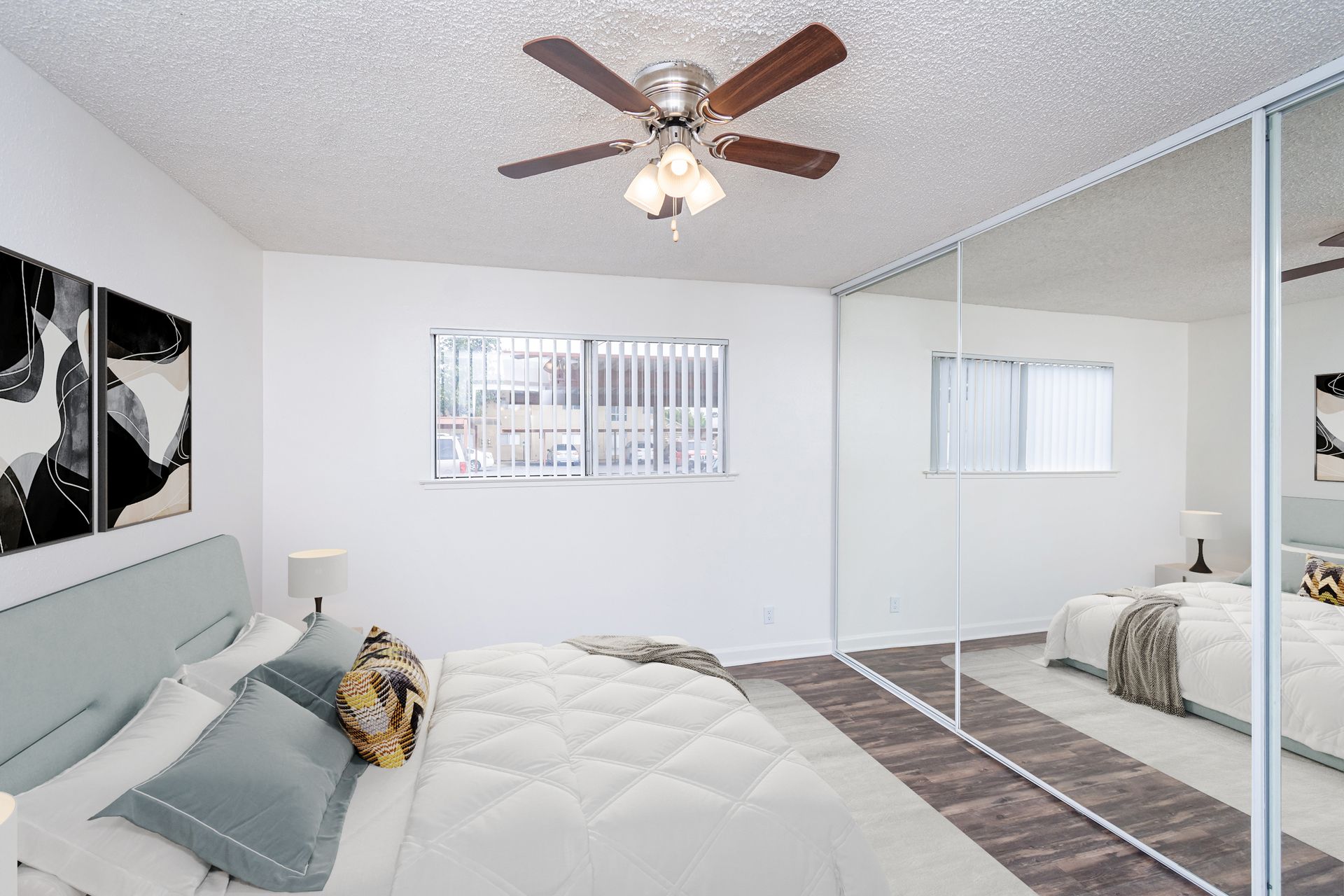 A bedroom with a bed , mirrors , a ceiling fan and a window.