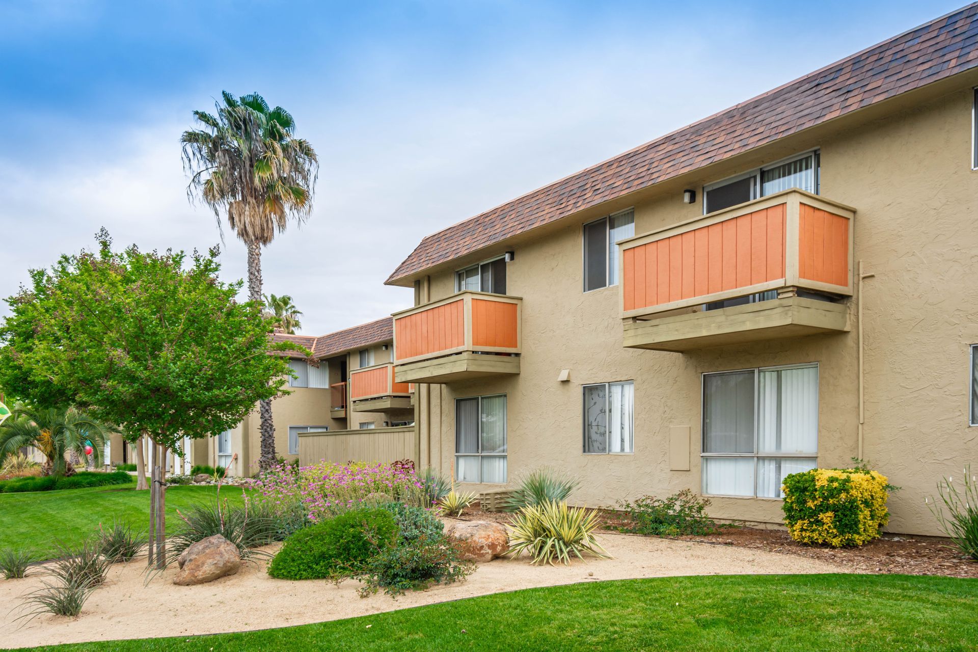 A large apartment building with orange balconies and a palm tree in the background.