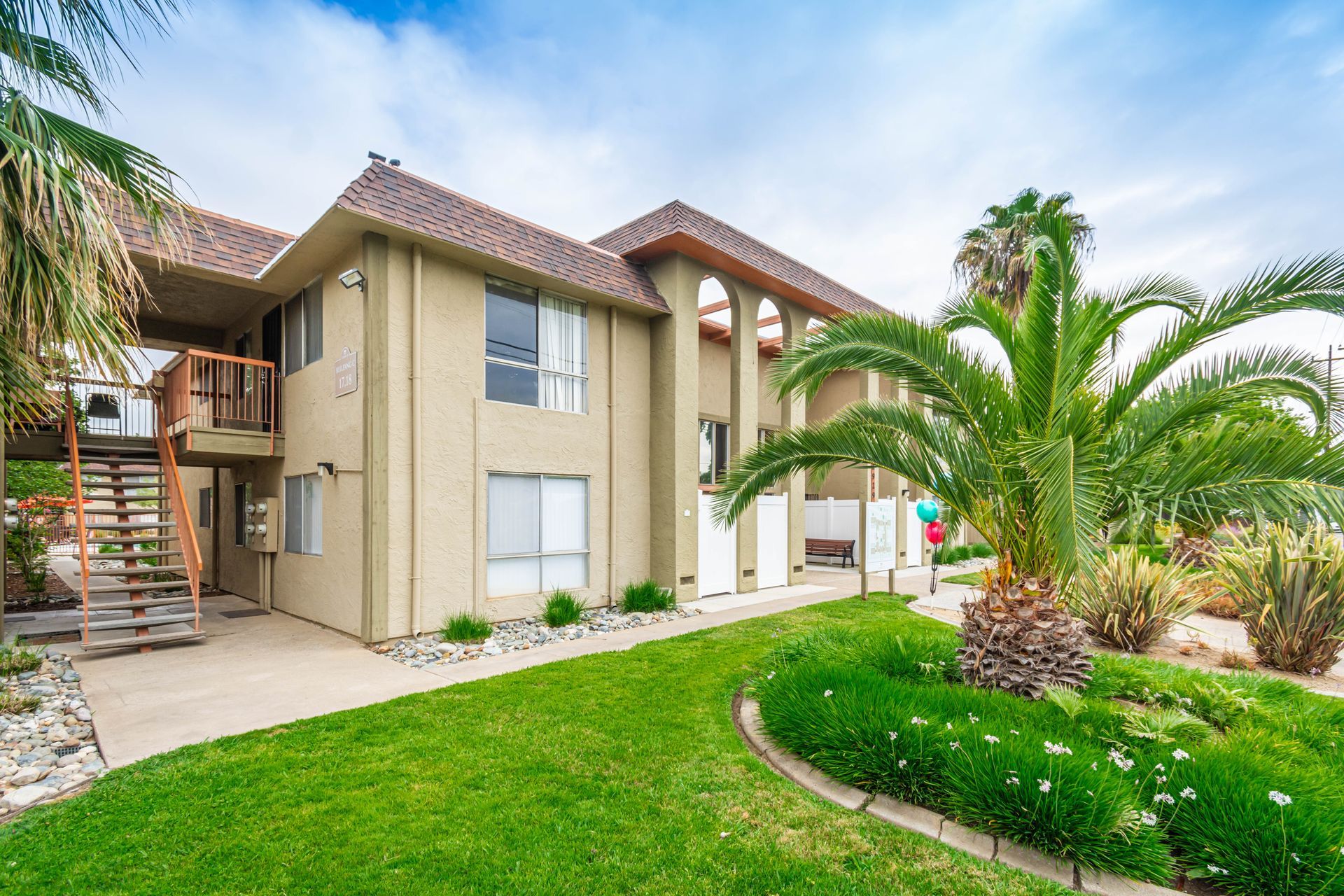 A large apartment building with a lush green lawn and palm trees in front of it.
